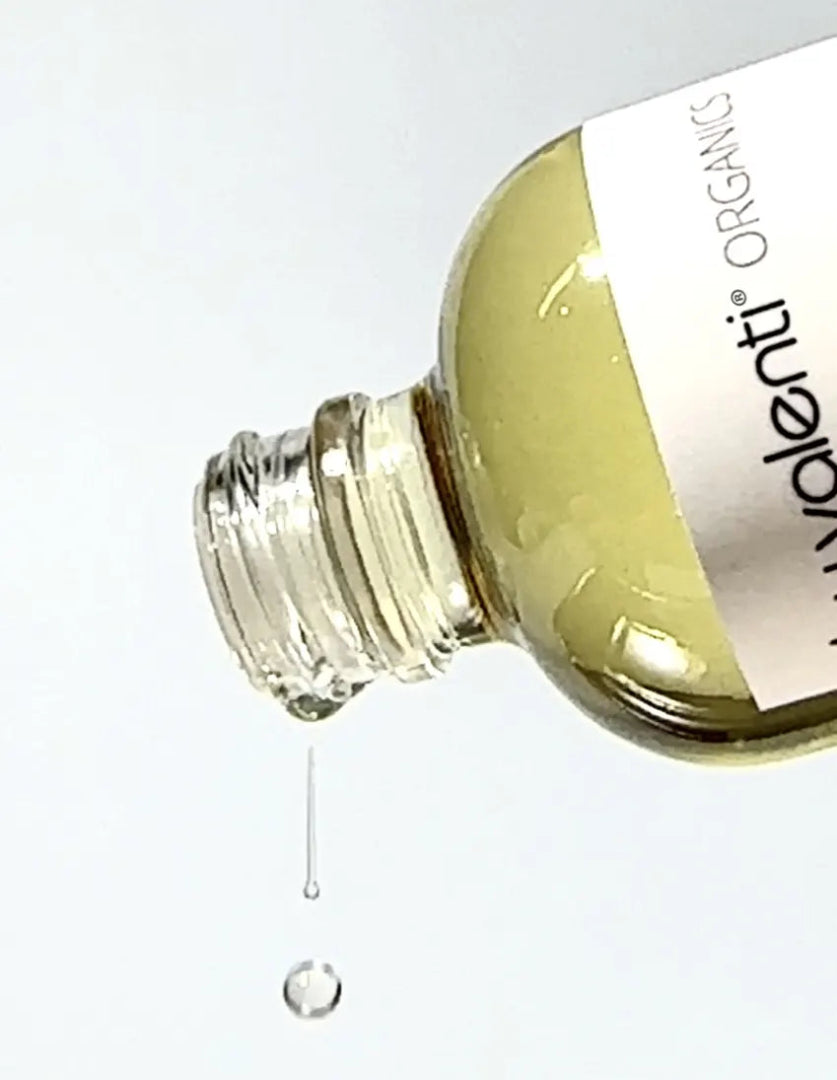 Close up of By Valenti body oil dropping with a light gray background