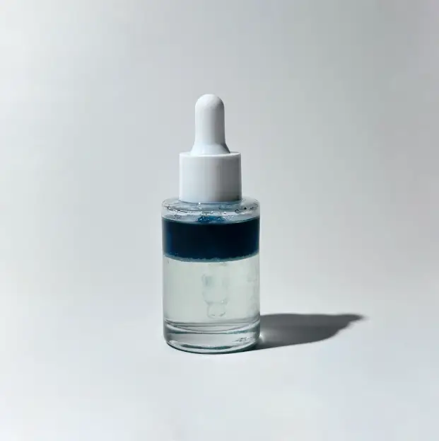 Glass dropper bottle with a blue and clear BY VALENTI biphase brightening serum with white cap on a light gray background