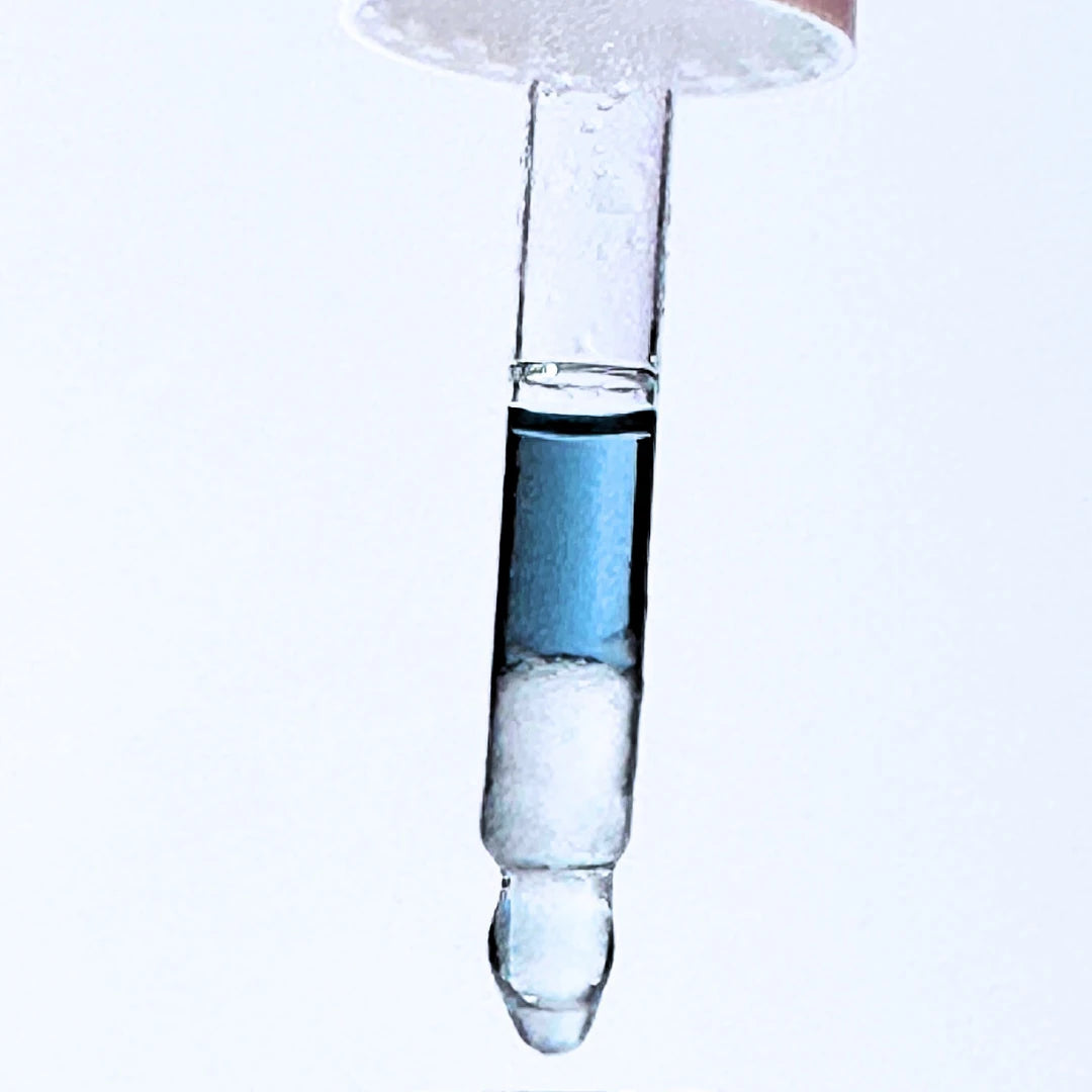 Close-up of a glass dropper with blue By Valenti bi-phase brightening serum on a white background
