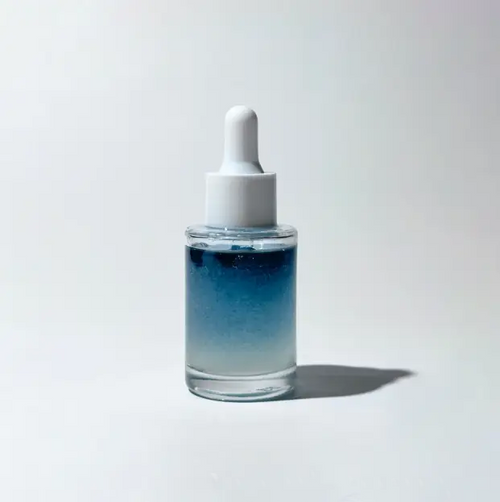 Glass dropper bottle with BY VALENTI blue bi-phase brightening serum on a light gray background