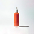 Glass bottle with dropper of By Valenti pink orange shimmering body oil on a white background