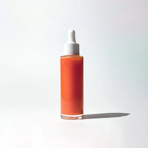 Glass bottle with dropper of By Valenti pink orange shimmering body oil on a white background