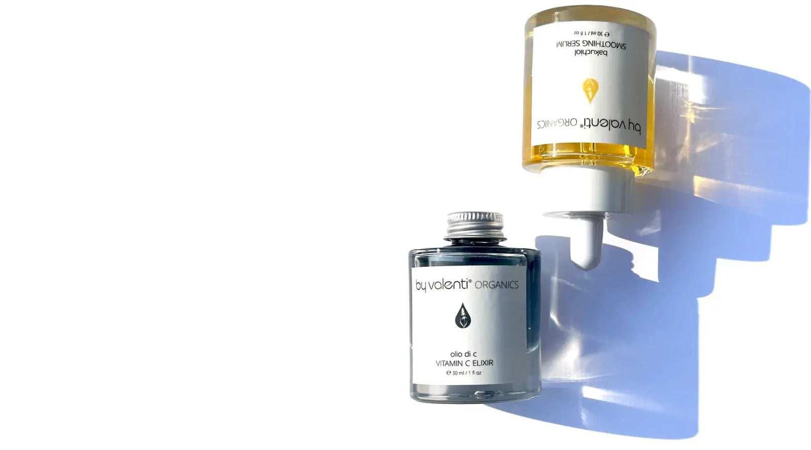Two glass bottles of By Valenti Bakuchiol serum golden color, and Vitamin C serum blue casting a long shadow on a white background