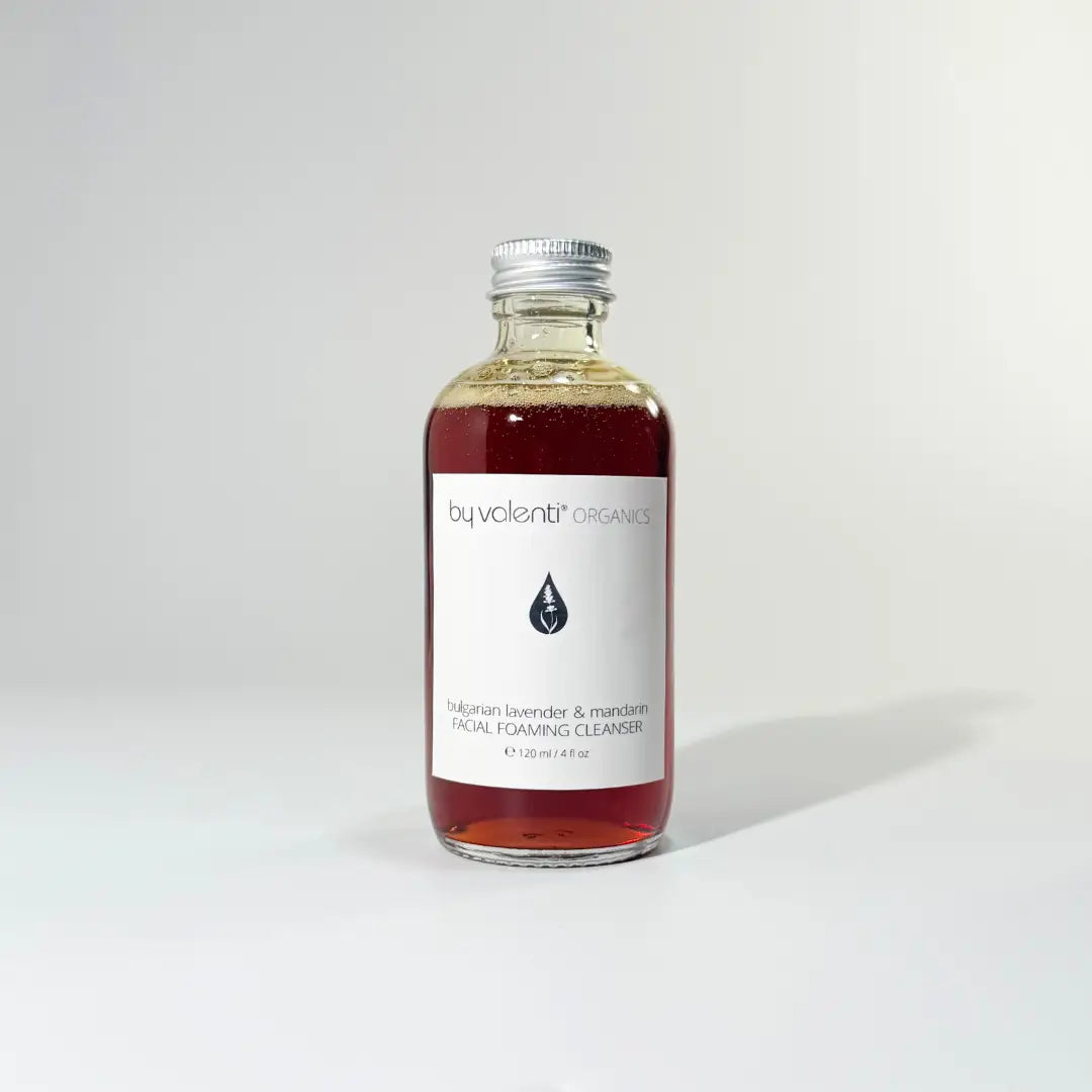 Glass bottle of BY VALENTI beautifully dark amber colored lavender face foaming cleanser with aluminum cap over white background