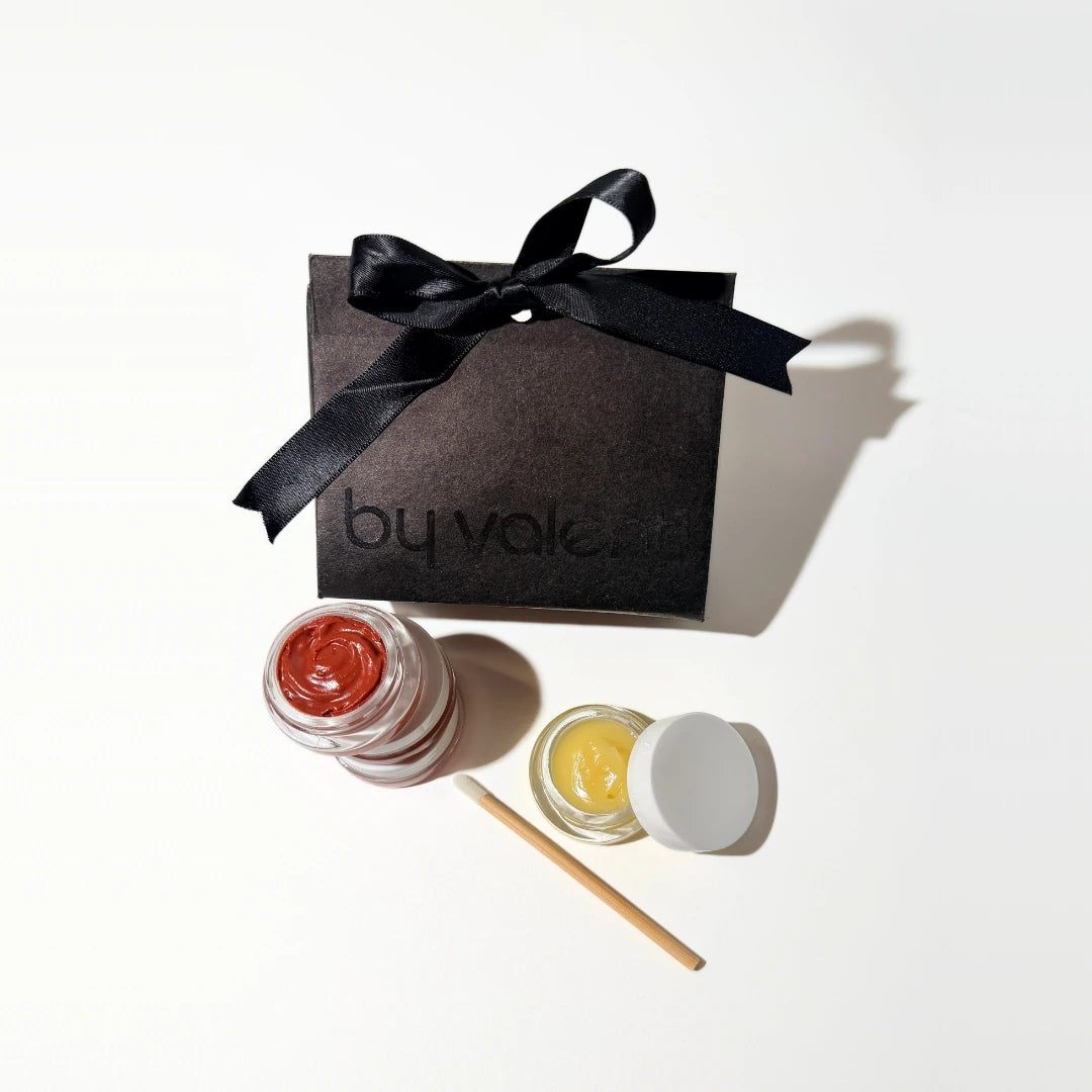 Two small jars of lip balm with a black box labeled 'by valenti' on a white background