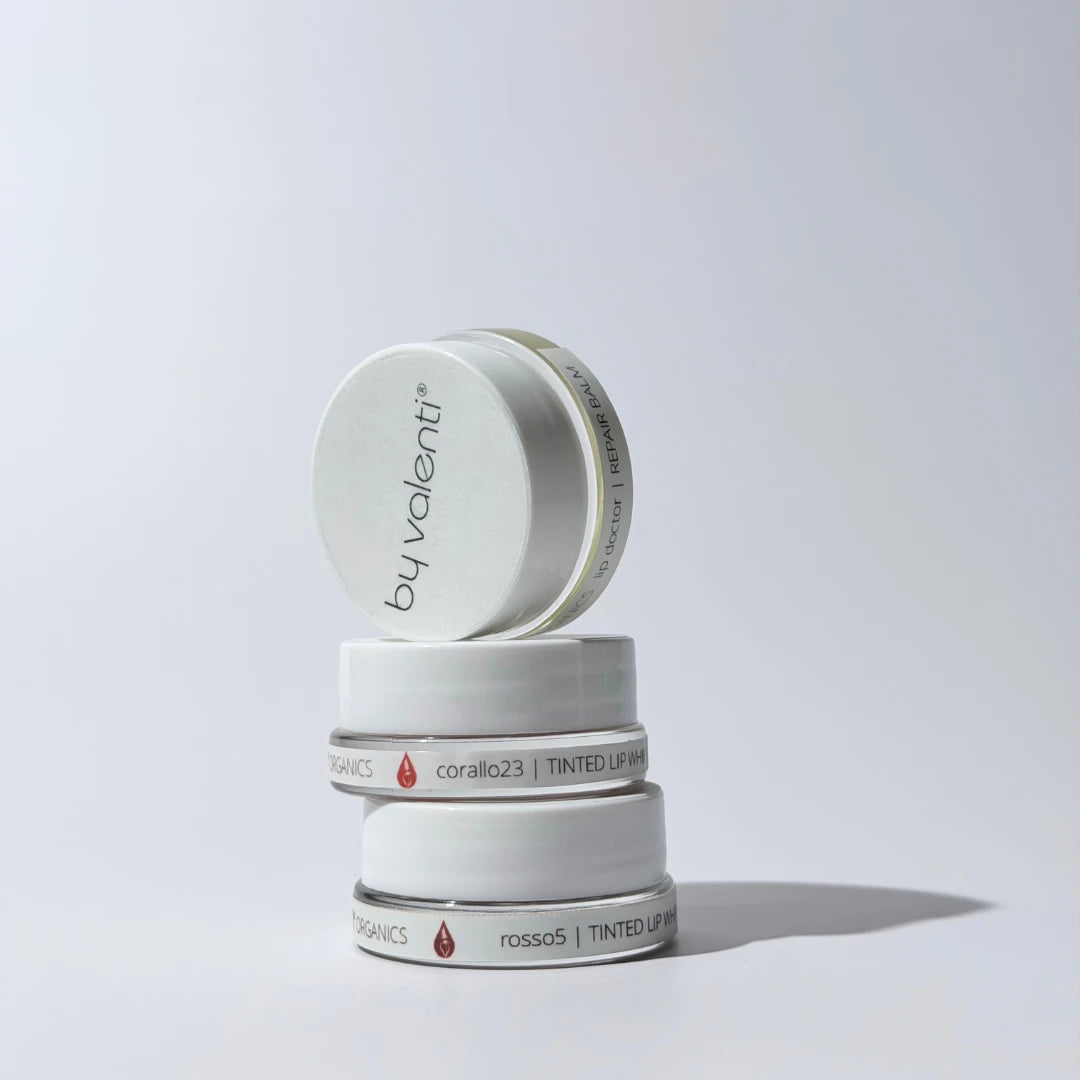 Stack of By Valenti Tinted Whipped Lip Balms containers with 'by valenti' branding on a light gray background