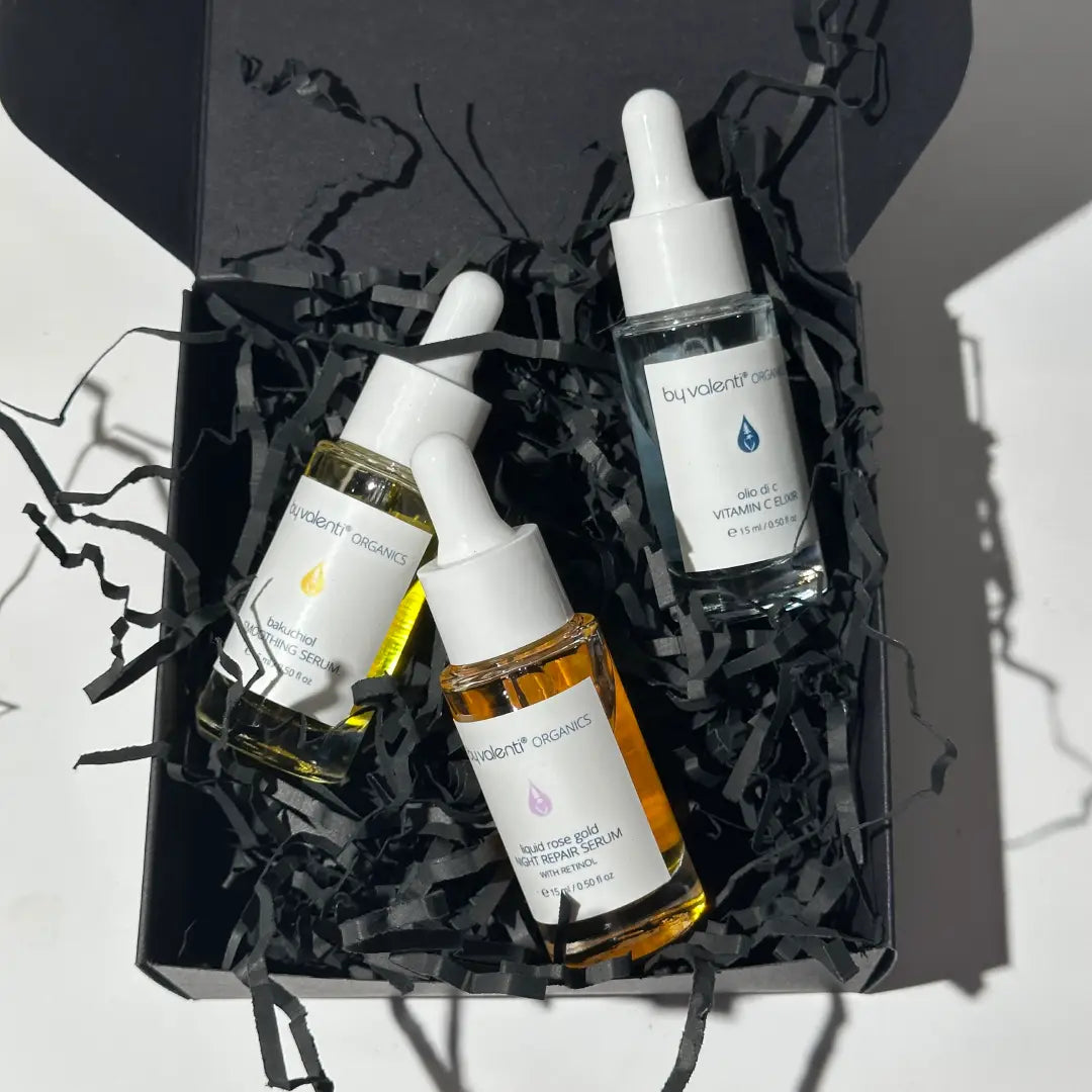 Three By Valenti gold, orange and blue skincare serum bottles in a black gift box with black tissue paper.