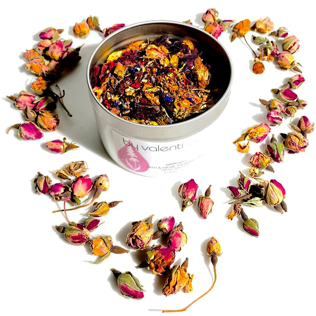 Colorful dried flowers in a white container with 'by valenti' branding, surrounded by more flowers on a white background.