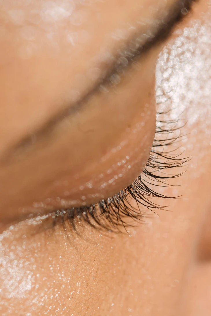 Close-up of a woman's eye after applying face serum near her eyes and skin.